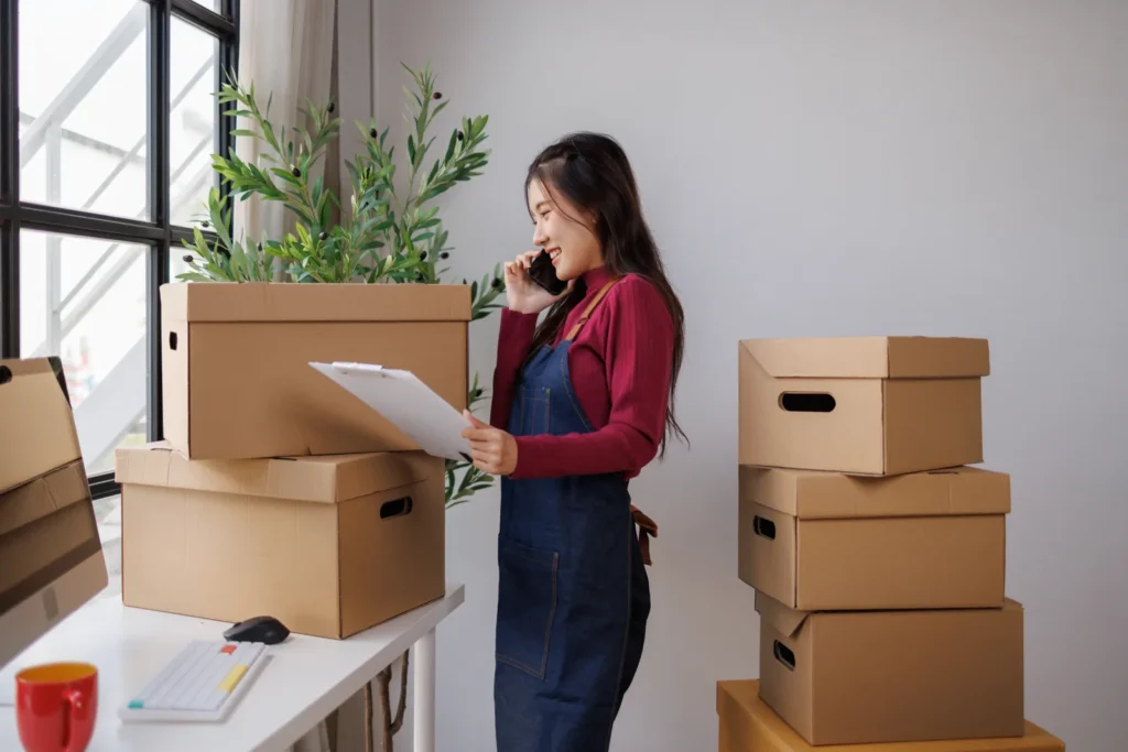 Business owner reviewing paperwork beside moving boxes in a bright workspace.